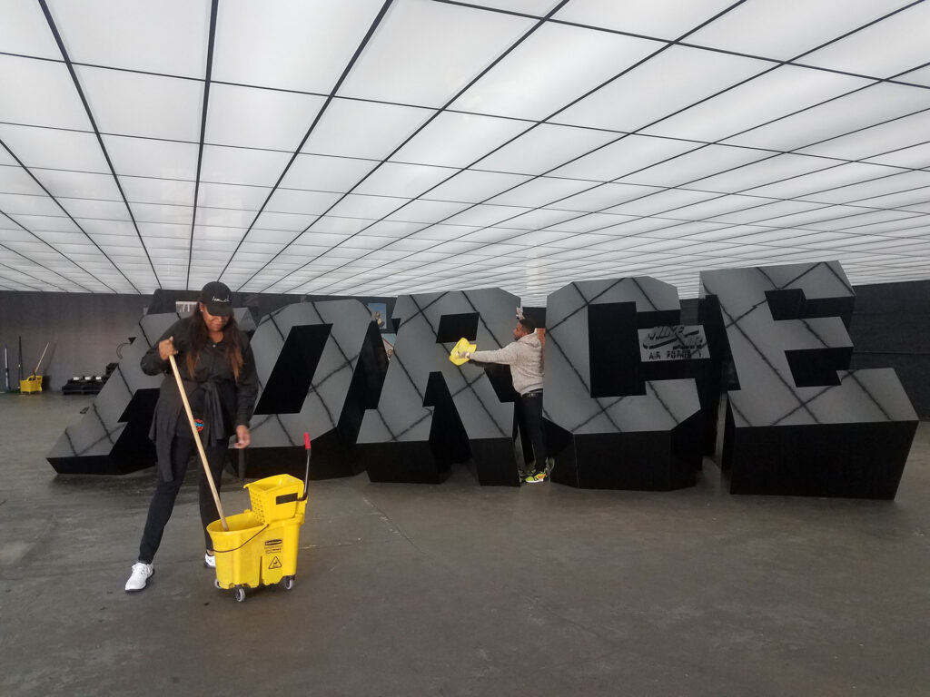 Two cleaners cleaning a FORCE sign at a Nike Branding activation.