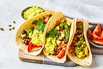 Three vegan tacos with guacamole, tomatoes, lettuce and black beans.