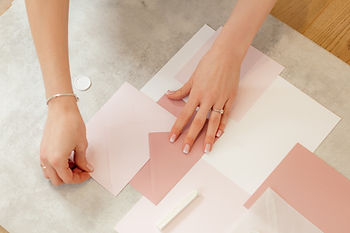 Female hands putting together pink invitations into darker pink envelopes.