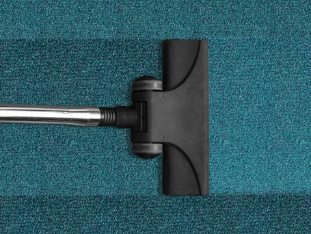 A black plastic roller vacuum sweeping across a turquoise carpet.