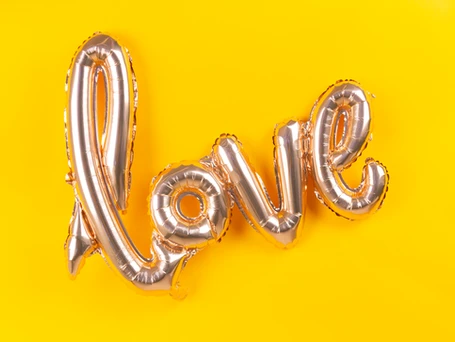 A mylar balloon spelling out the word "love" in front of a canary yellow background.