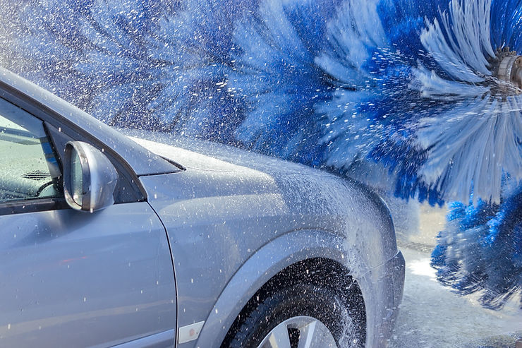 A blue car moving through a car wash with blue fuzzy scrubbers whirling across the front hood.