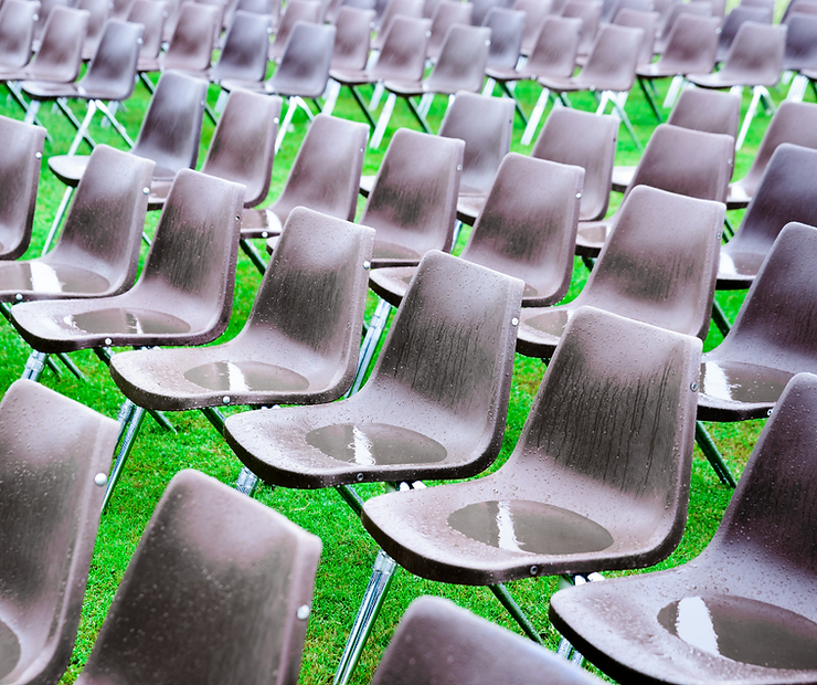 Rows of black plastic chairs lined up in a field of clipped green grass with rain puddles in the seats.