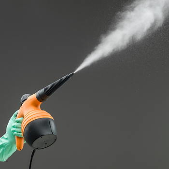 Disinfectant spray coming out of an orange sprayer held by a green gloved hand.