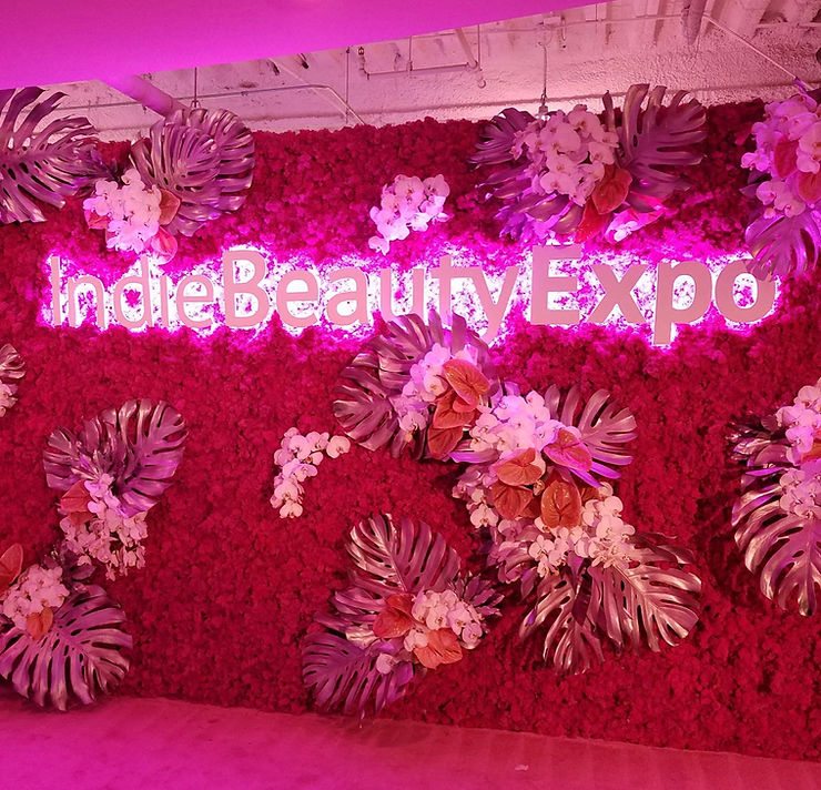 Indie Beauty Expo sign with pink lighting against a floral wall sprayed dark pink