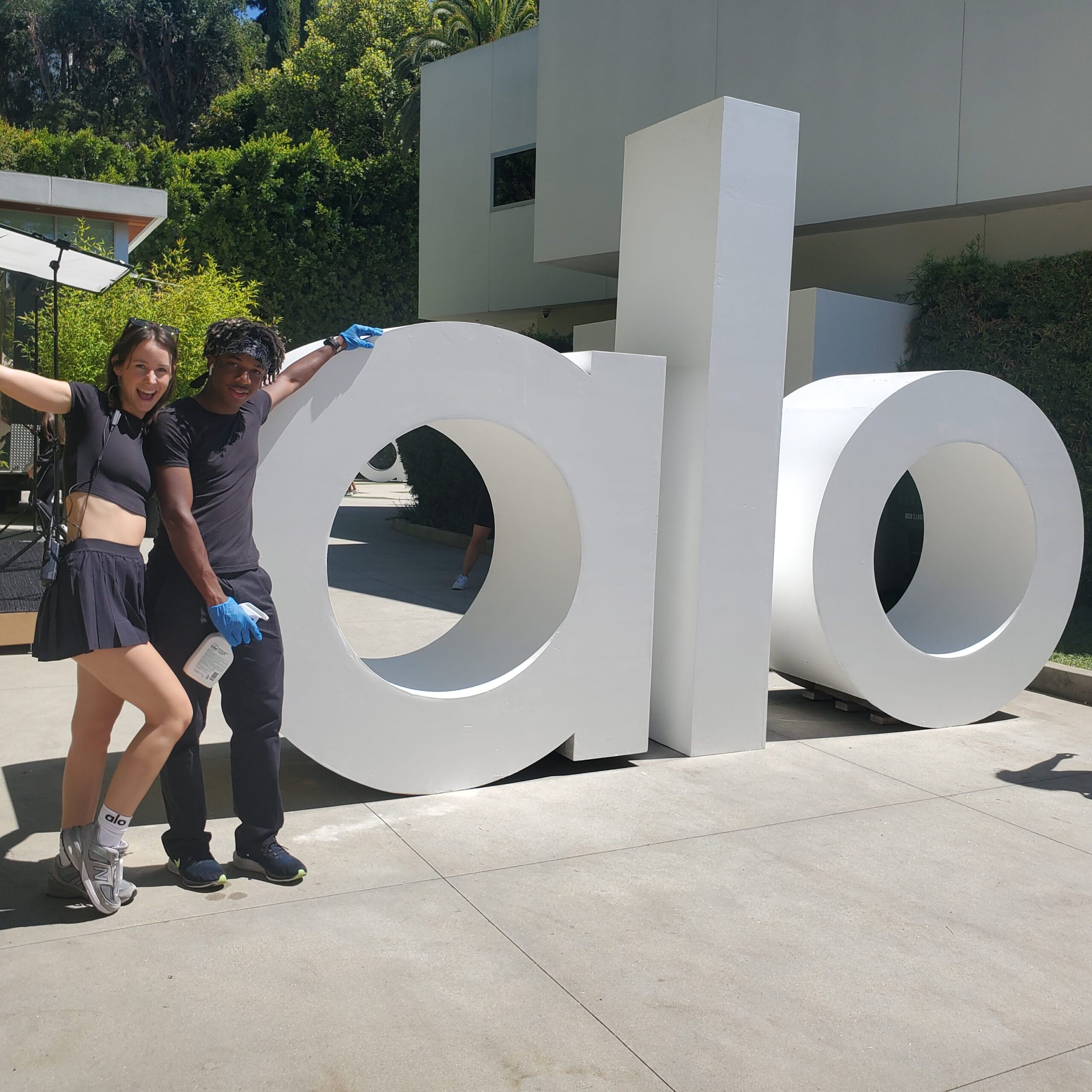 A PopUp CleanUp cleaner posing with an event goer in front of the alo yoga sign at an alo yoga branding activation