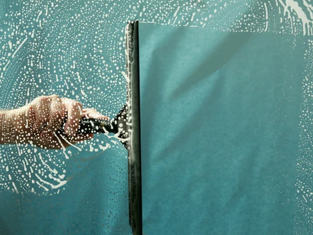 A squeegee wiping soapy solution off a window.