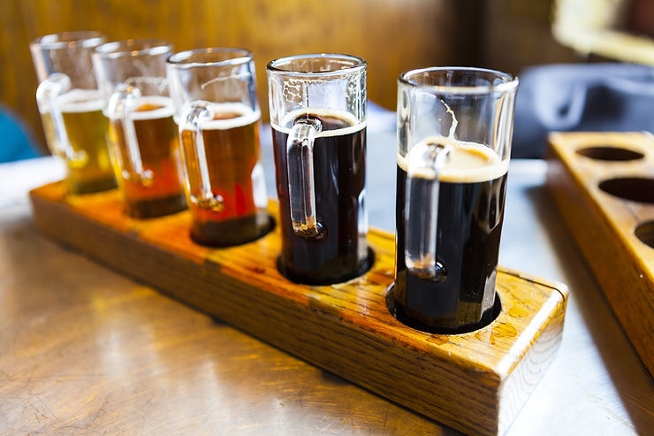 A wooden tray with holes for five different kinds of beer ranging from really dark to amber to really light yellow.