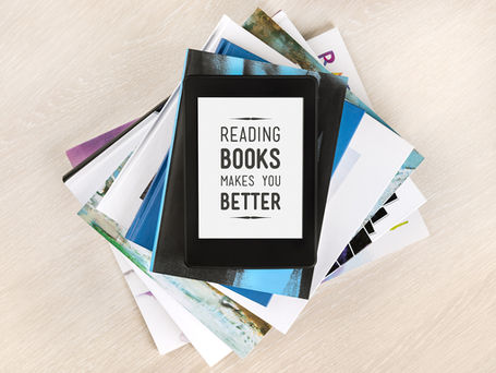 A pile of books. ON top is a printed sign reading "Reading Books Makes You Better."