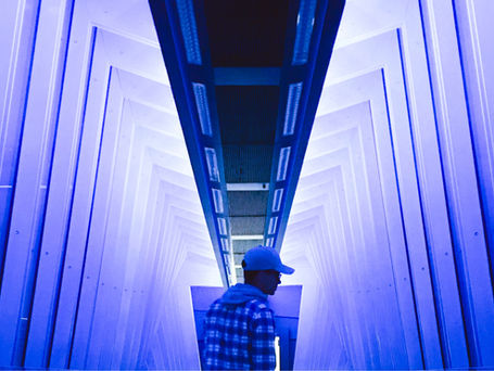 A man standing in a series of geometrically rectangular arches lit with UV light.