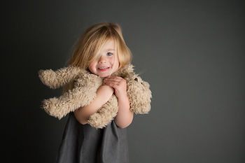 A little blonde haired blue eyed girl holding a stuffed teddy bear.