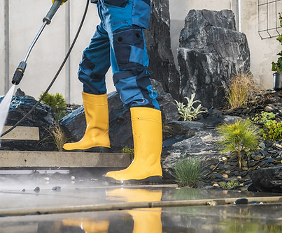 A man in blue jeans and yellow waterproof boots power washing concrete steps.