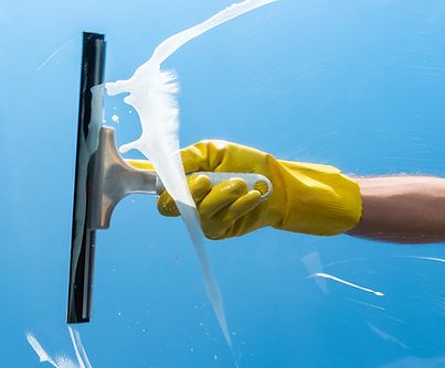 A yellow gloved hand pulling a squeegee across a window during window cleaning.