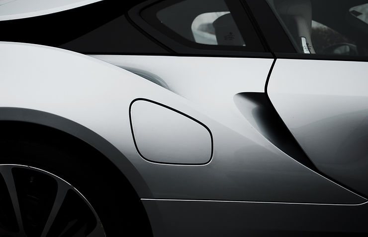 Exterior section of a steel grey sports car with part of the windows, wheel and gas tank.