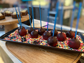 Chocolate cake pops with colored sprinkles in front of chocolate mousse cups topped with whipped cream.