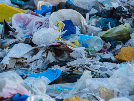 Plastic trash strewn outdoors with torn and broken plastic bags, plastic bottles, and used food wares.