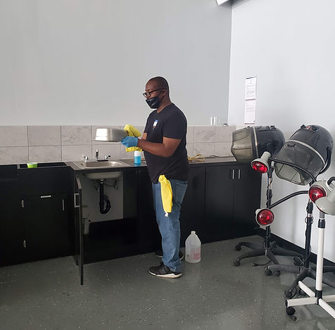 One of PopUP CleanUP's cleaners scrubbing stainless steel hardware at a hair salon with mobile hair dryers lined up behind him and a sink to the side of him.