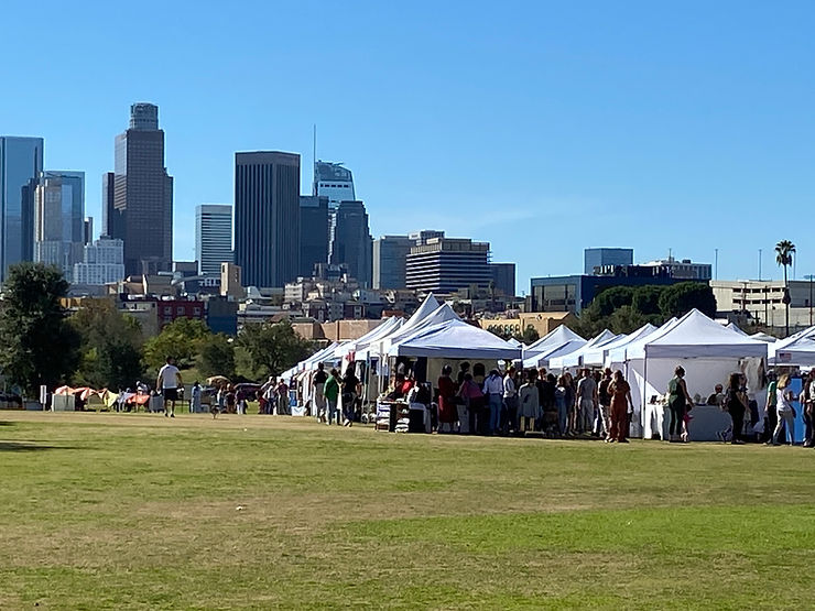 A view of the Renegade Craft Fair at Los Angeles State Historic Park beyond which rise the skyscrapers of Downtown Los Angeles.