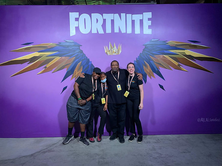 The PopUP CleanUP crew standing in front of a mural of metal wings and a metal crown under the Fortnite logo.