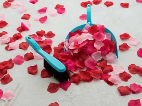 A turquoise dustpan and brush sweeping up light pink and fascia rose petals.