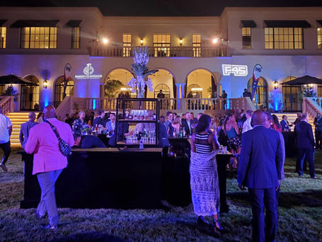 Partygoers congregating in a backyard of a Beverly Hills Mansion for a branding activation with sponsors like F45 and Relais Chateaux projected on the mansion walls.