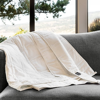 A white Baloo weighted blanket draped over a grey sofa.