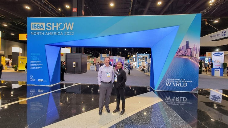 CEO Kenetia Lee with Operations Manager Steve at the 2022 ISSA Show in front of a big blue printed welcome arch.