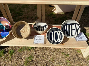 Ceramic bowls for cats and dogs with the words "FOOD" and "WATER" in them on a wood shelf at the Renegade Craft Fair.