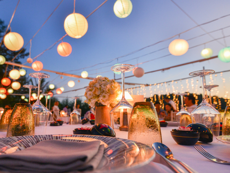 Outdoor banquet with chinese lanterns strung overhead and flowers and place settings adorning the tables.