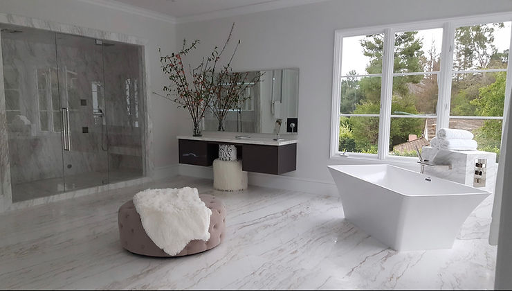 A swanky bathroom at a Beverly Hills Estate with a standalone white tub, glassed in shower, cushion, and modern vanity with marble tile floors.