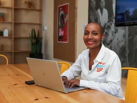 PopUP CleanUP CEO Kenetia Lee seated in a metal yellow chair in front of a laptop computer at a wooden table