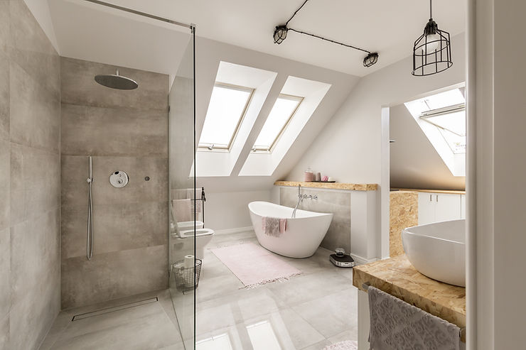 A swanky private bathroom with an oval stand alone tub, glass shower with expensive fixtures and large marble tile walls, and a beautiful skylight with plenty of light flooding through.