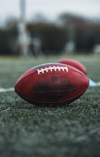 A regular National Football League football resting on green grass on a football field.