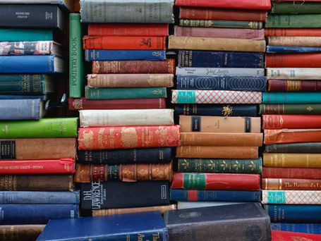 Old leather bound books piled up in stacks with their aged and torn spines facing outwards.