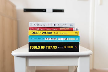 A pile of self-help books including OUTLIERS, CRUCIAL CONVERSATIONS, DEEP WORK, GETTING THINGS DONE & TOOLS OF TITANS.