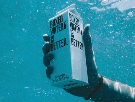 A hand holding under water a carton of boxed water printed with the label BOXED WATER IS BETTER