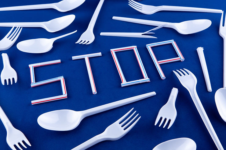 White plastic utensils scattered on a dark blue background with cut up straws spelling out the word "STOP."