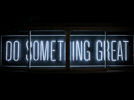 A white neon sign that says DO SOMETHING GREAT against a black backdrop