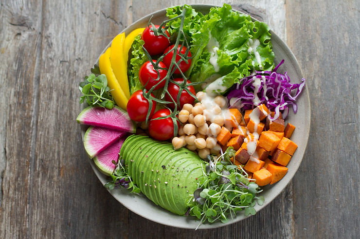 A bowl of vegetables including watermelon radishes, avocado, cherry tomatoes, diced yams, and chickpeas on a bed of green leaf lettuce and shredded purple cabbage.  Sunflower sprouts garnish the outsides of the plate.