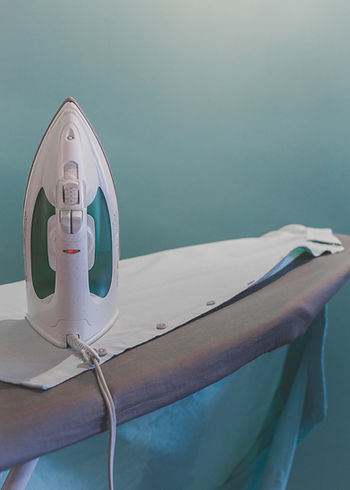 An iron sitting upright on an ironing board.