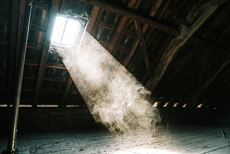 A dark wooden attic with a single skylight window letting light illuminate oodles of dust in the air.