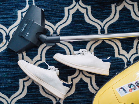 White sneakers and a yellow vacuum cleaner on a blue and white patterned rug.