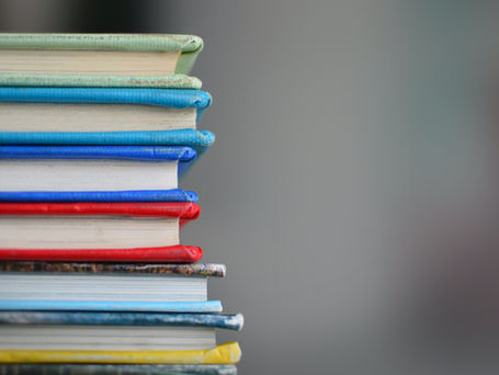 A stack of books with different colored covers, red, green, blue, yellow from the viewpoint of the paper.