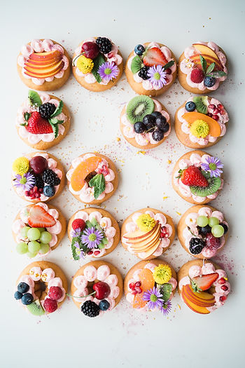 Canapé desserts garnished with colorful fruits like peaches, kiwis, blueberries, cherries, raspberries and strawberries.