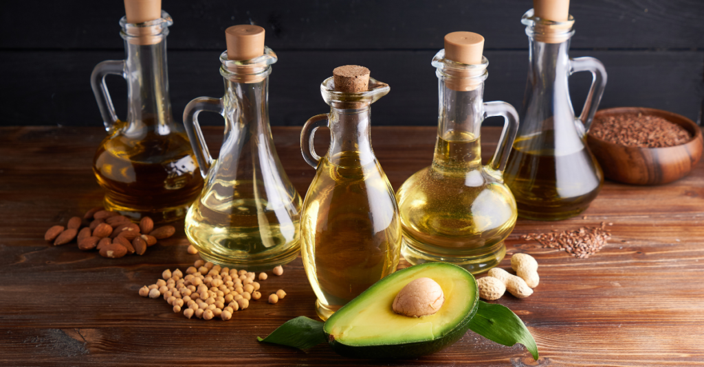 Five oil decanters with nuts and an avocado on a wood counter.