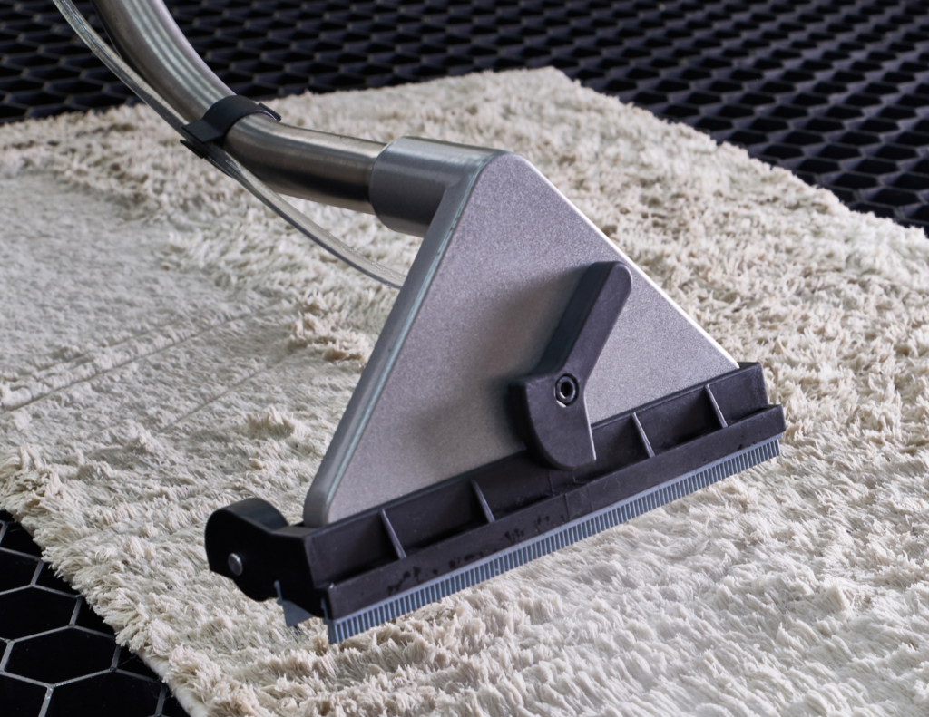 A modern grey vacuum extracting dirt and germs from white carpet.