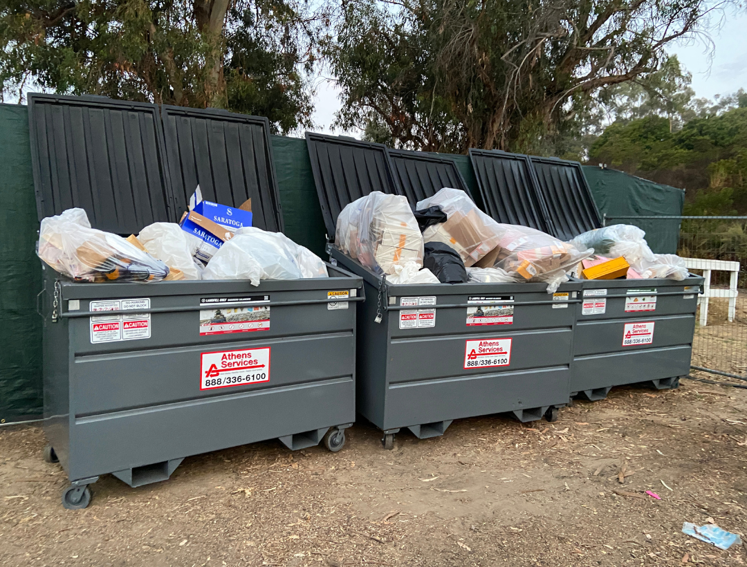 Three 3-cubic yard green dumpsters lined up in a row and overfilled with garbage.