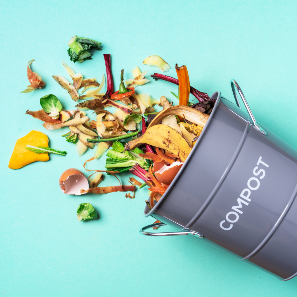 A grey metal bucket labelled compost with food scraps spilling out of it against. Composting is essential for sustainability.