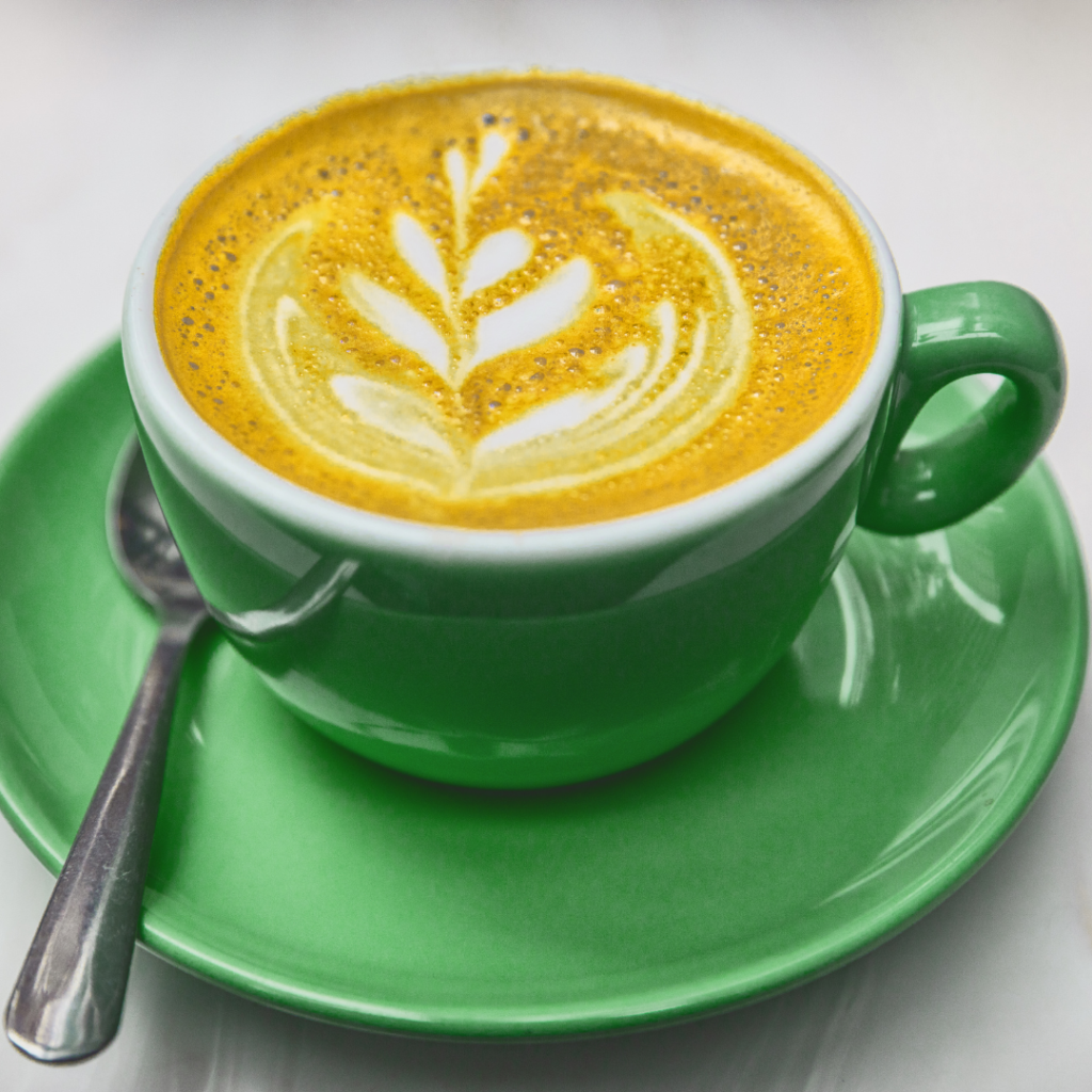 Tumeric Latte in a green ceramic cup on a green ceramic saucer and a stainless steel spoon on the saucer.