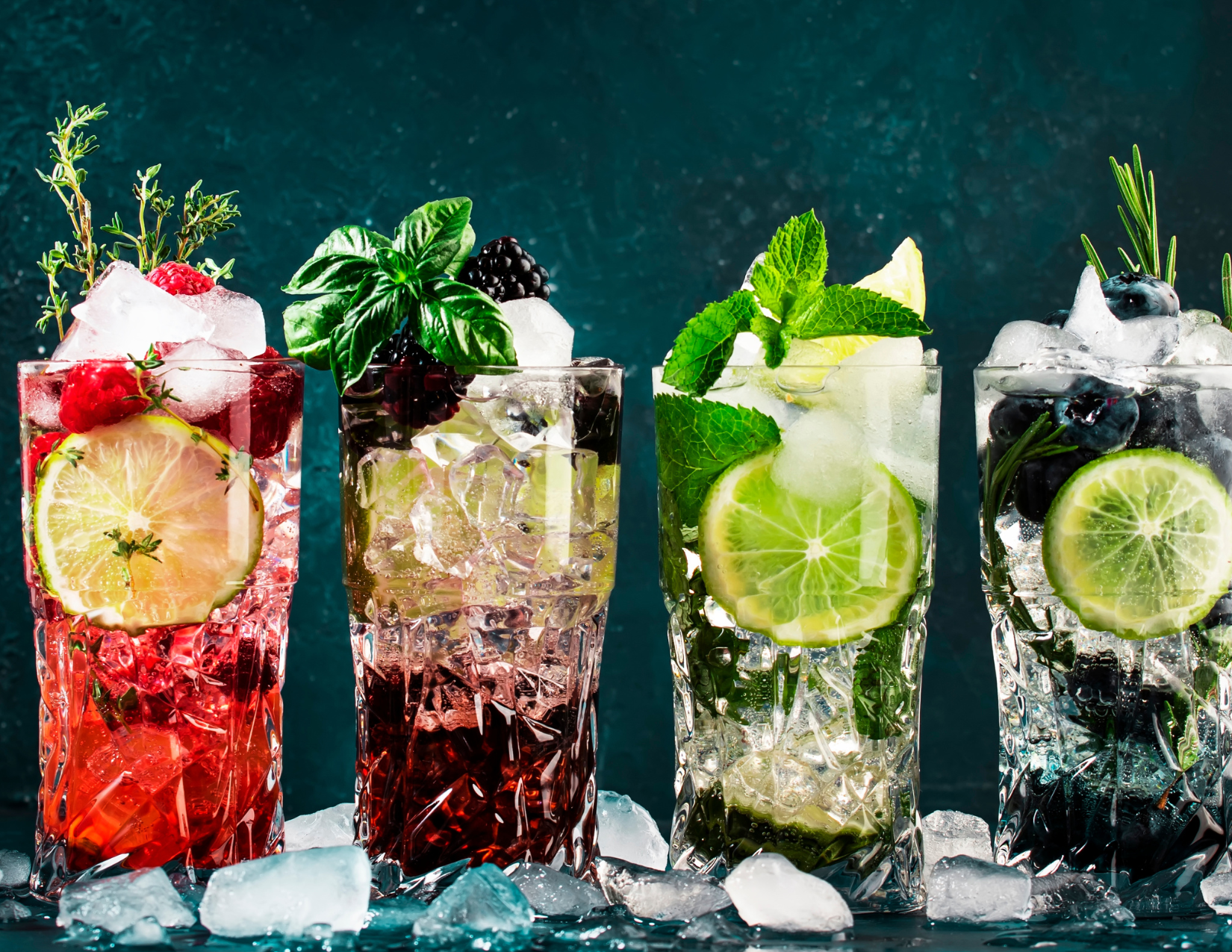 Sober Curious Event Drinks: A row of four mocktails garnished with different fruit: strawberries, limes, blackberries, blueberries.